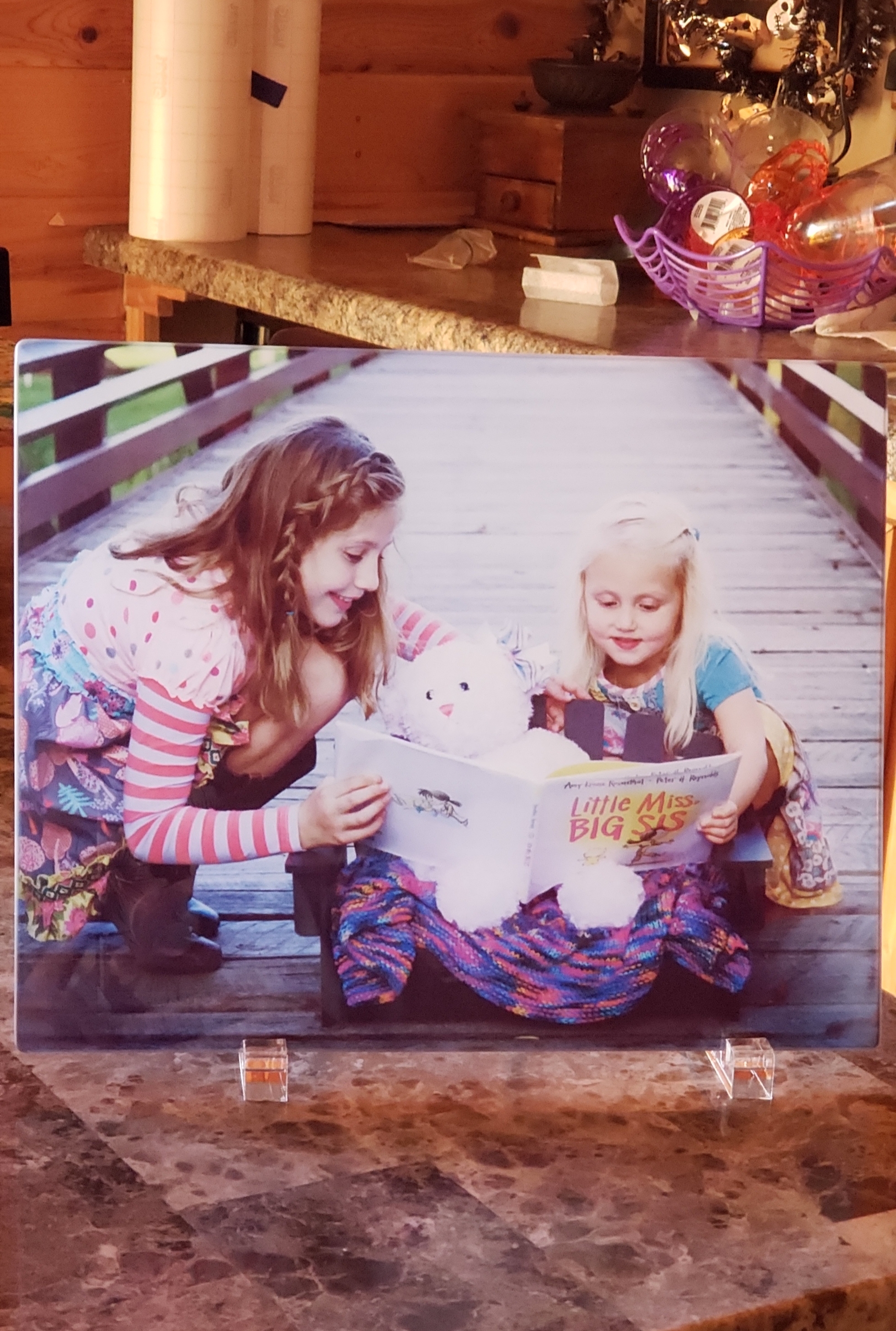 A photo showing two sisters reading a book to their baby sister in Heaven.
