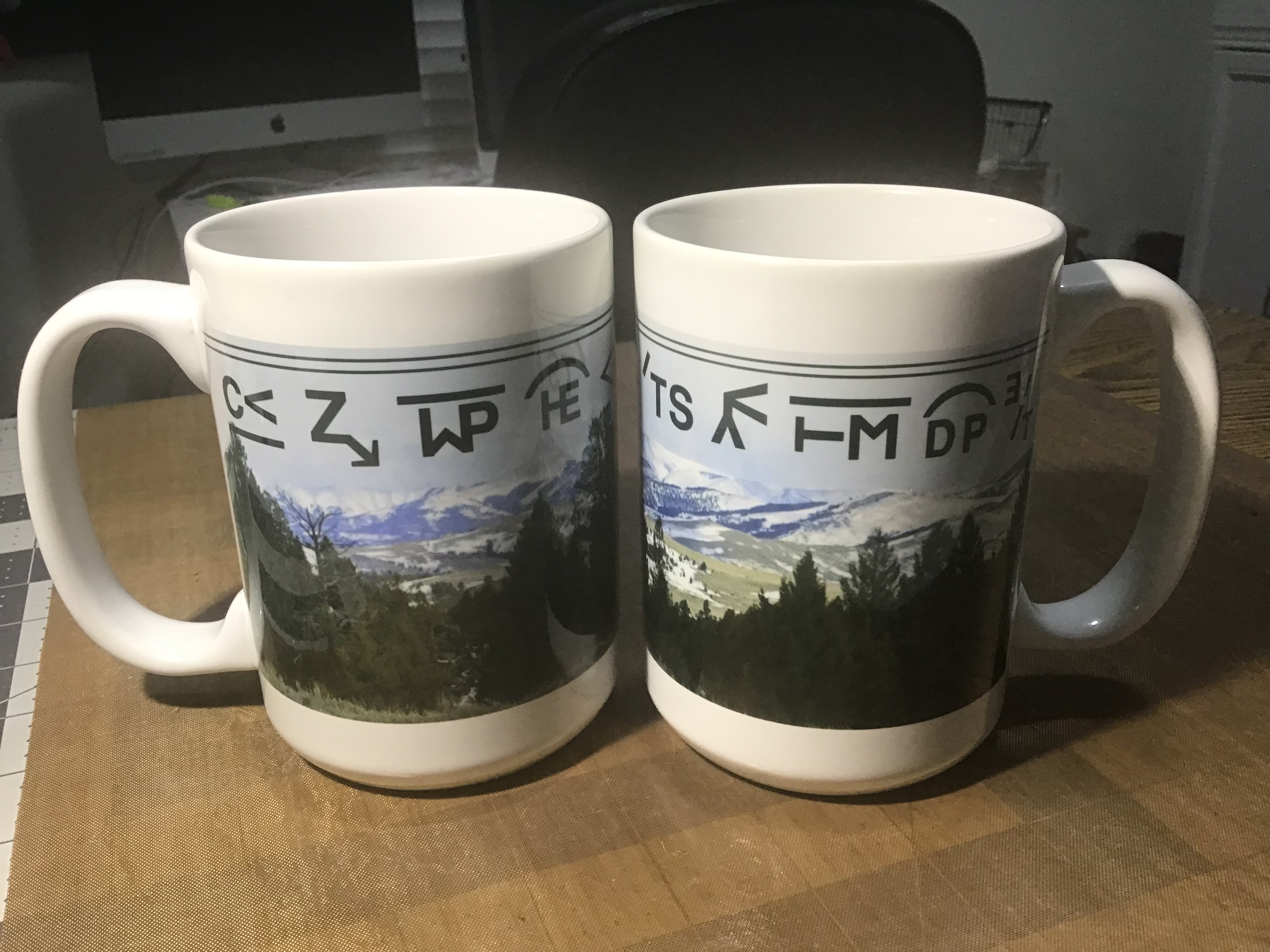 Mug featuring a Mountain scene with local ranchers state brand around top.